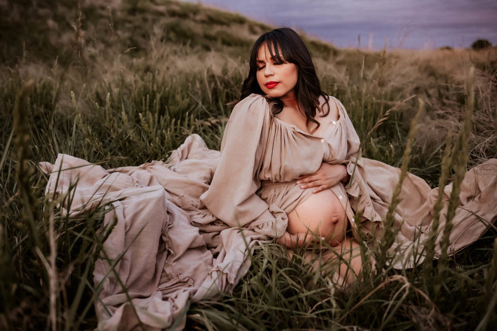 Springfield MO maternity photographer captures pregnant mom kneeling in open field hugging belly