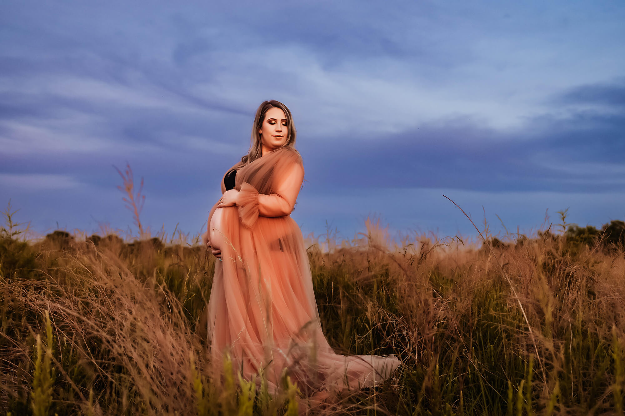 Springfield Mo maternity photographer captures mom in field holding her belly at sunset