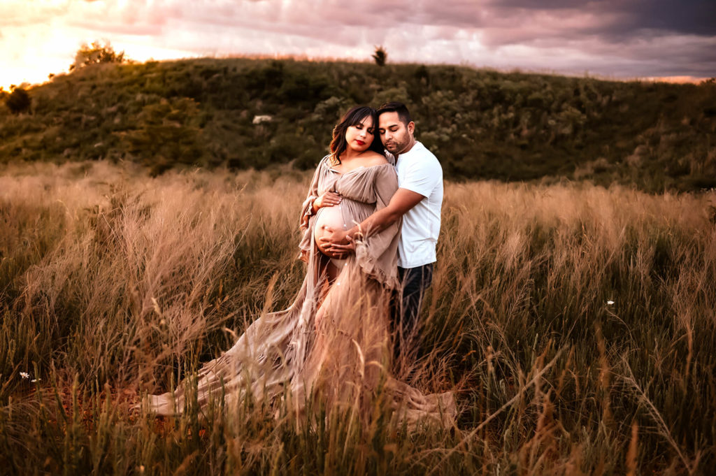 maternity pictures of couple cuddling in open field after visiting Cox OBGYN in Springfield MO