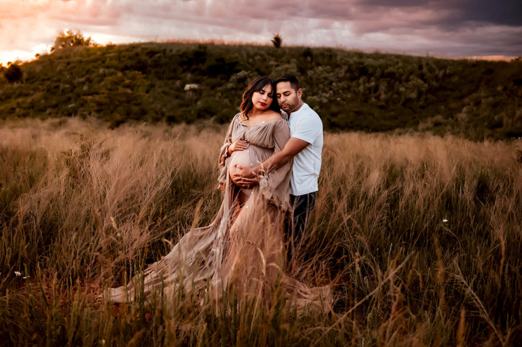 pregnant couple cuddling in field in Kansas City