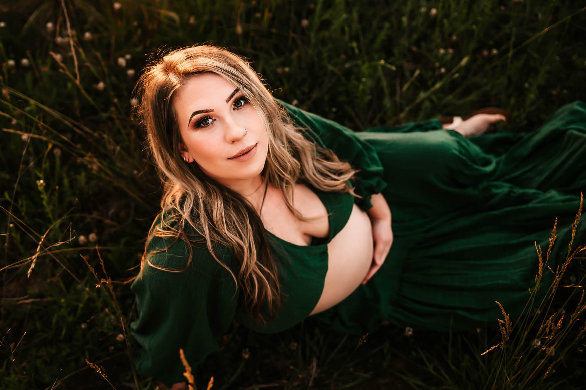 Springfield MO maternity photographer captures pregnant mom sitting on field holding belly