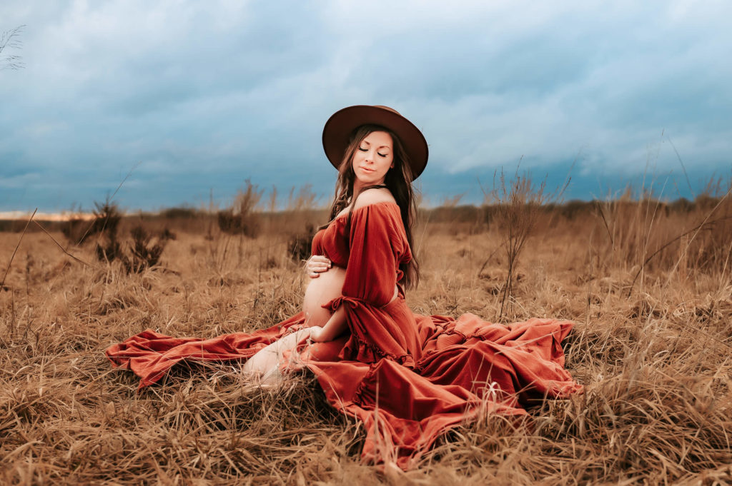 maternity photographer in Springfield MO captures pregnant mom kneeling in field hugging her belly