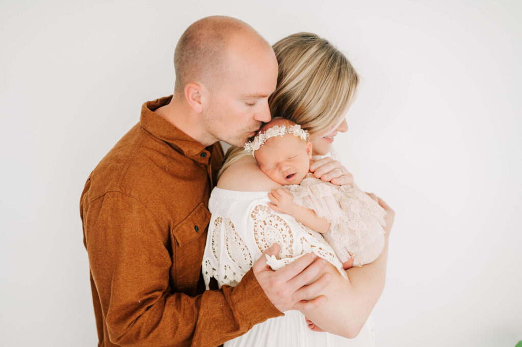 Springfield MO newborn photography of dad kissing baby on mom shoulder