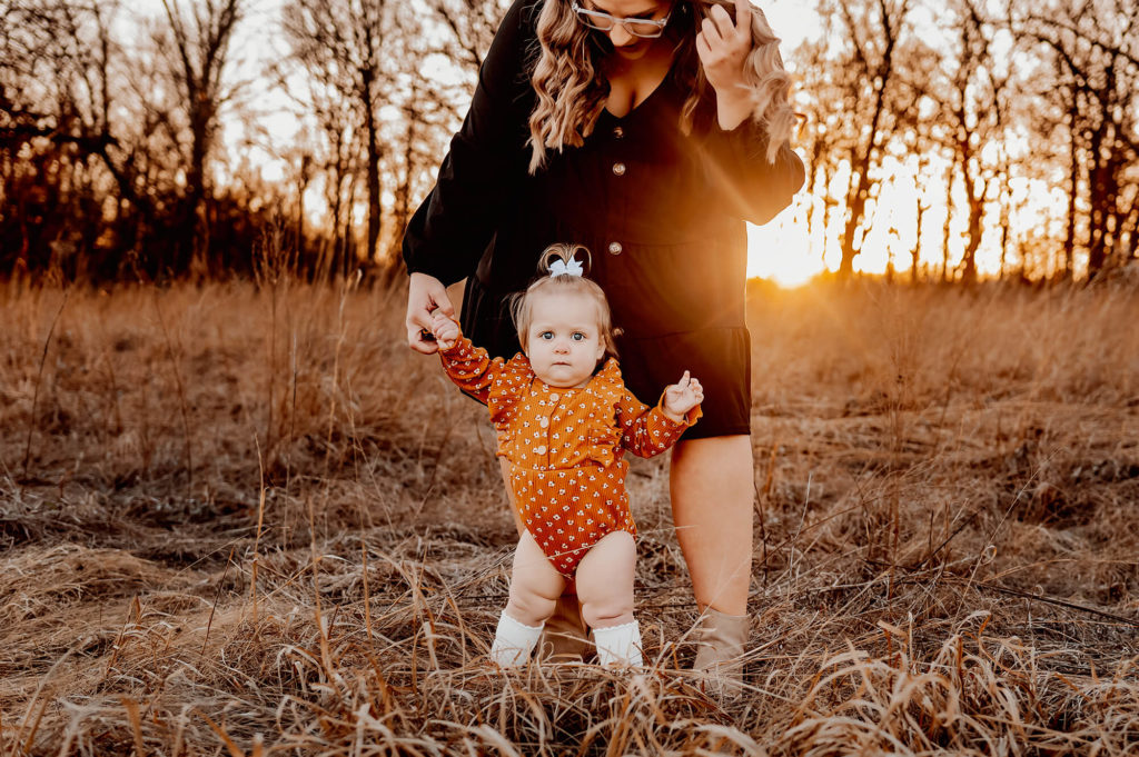 professional family photographer in Springfield MO captures mom and baby girl standing in field at sunset