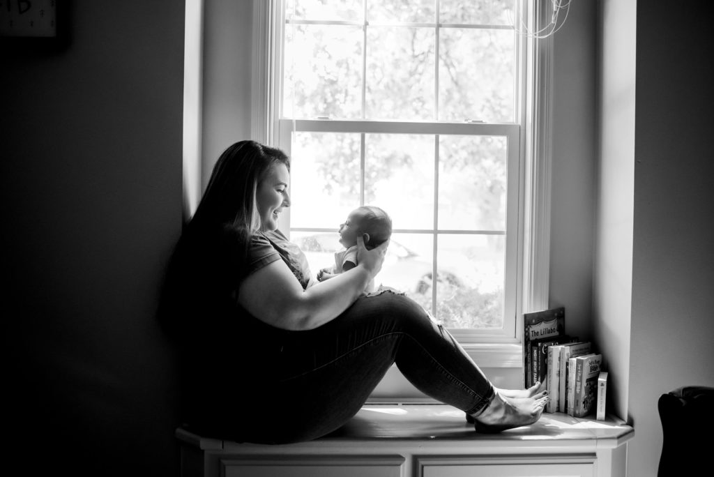 baby photographer in Springfield MO captures mom holding newborn baby while sitting on window bench