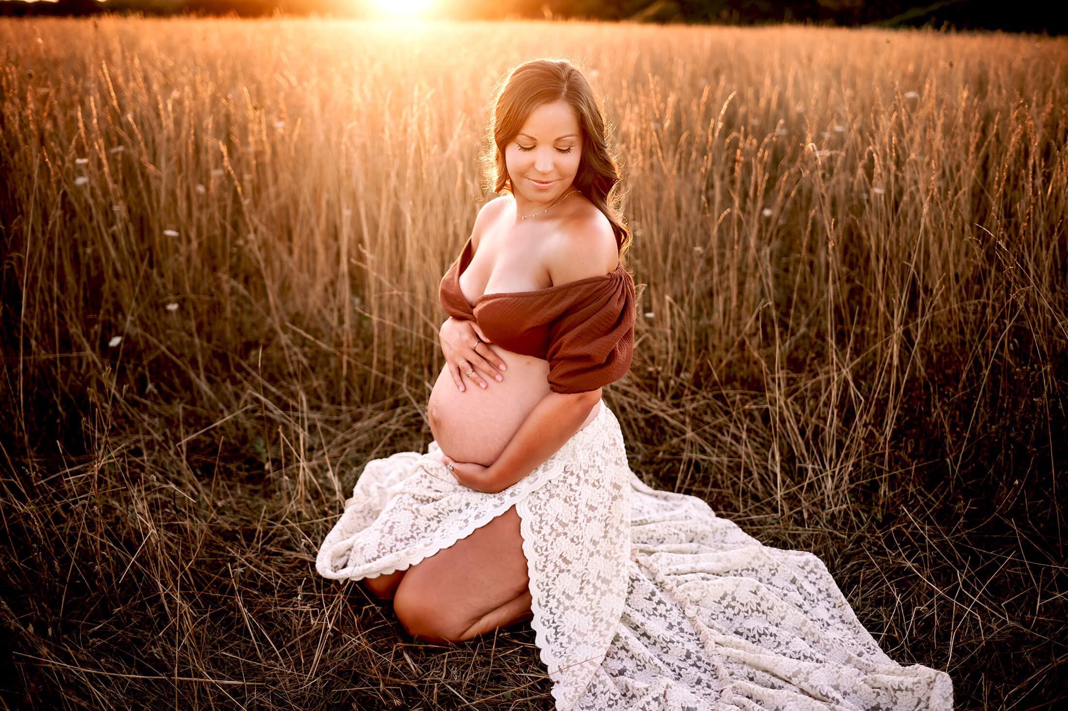 Springfield MO photographer captures pregnant mom kneeling in field after appointment at family birth and wellness in Springfield MO