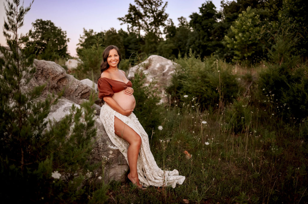 maternity photographer in kansas city captures mom sitting on a rock holding her bump