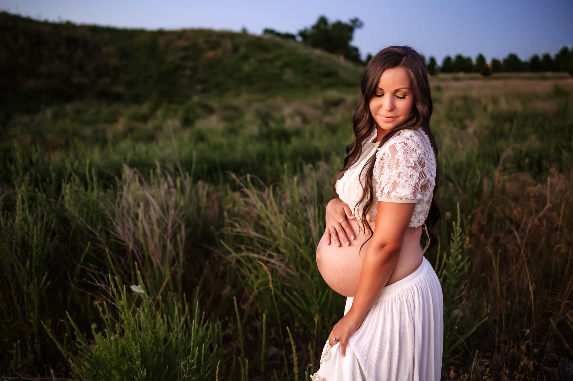 maternity pictures in Kansas City of pregnant mom in field at sunset holding belly