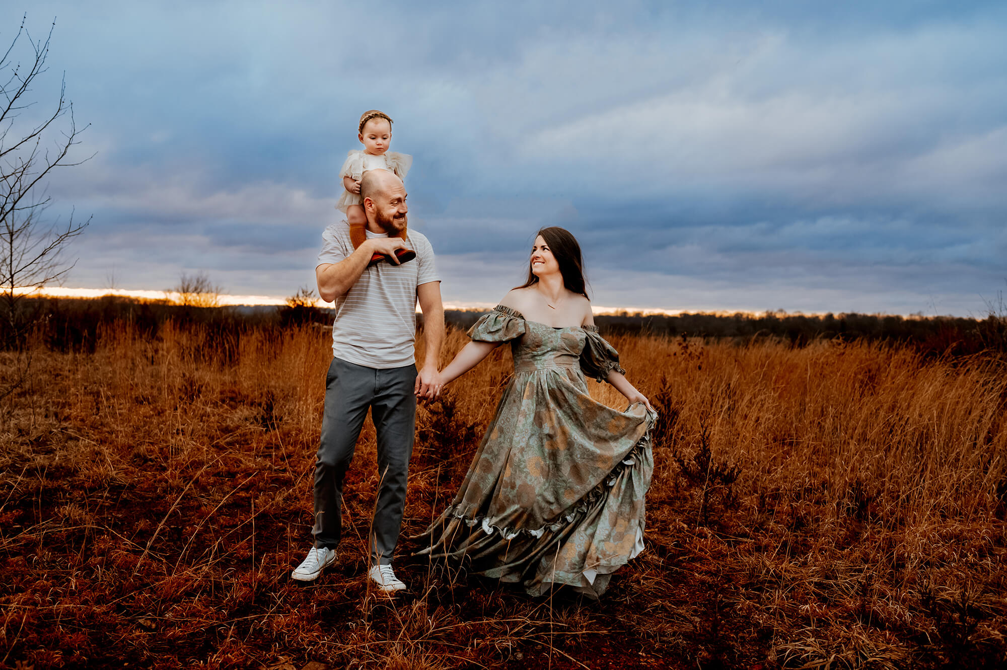 Springfield MO family photographer captures couple walking in field with toddler on dad's shoulder