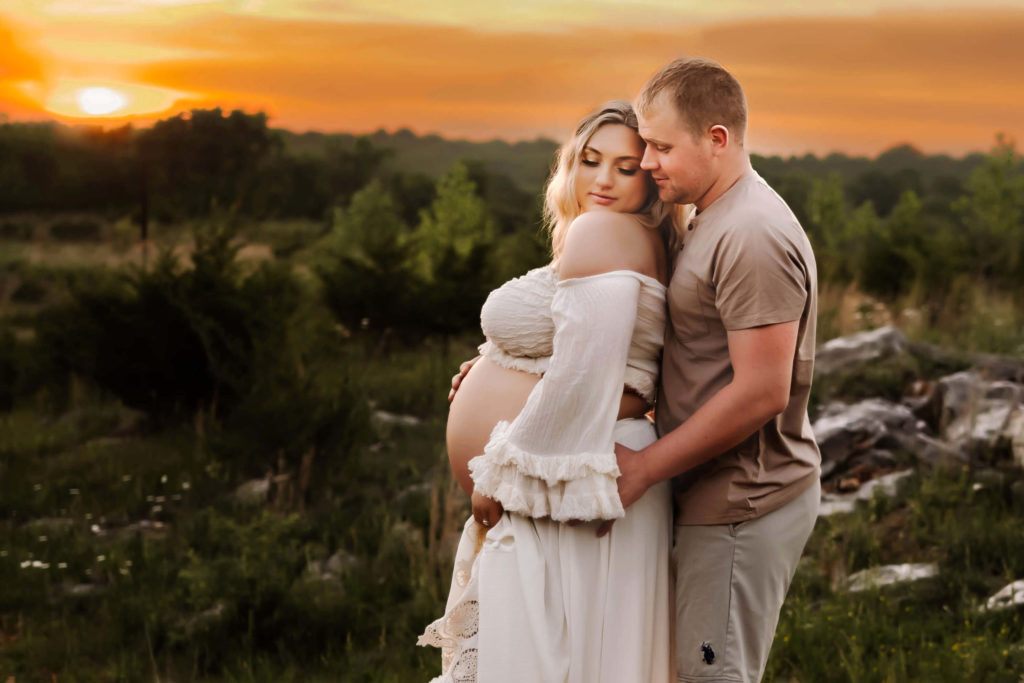 maternity photographer in Kansas city captures pregnant couple cuddling on rock at sunset