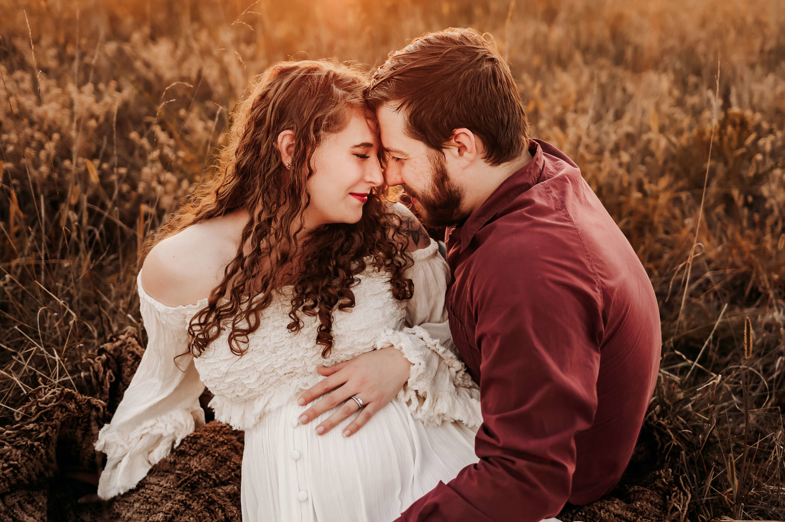 maternity photographer in Springfield MO captures pregnant couple cuddling while sitting in field