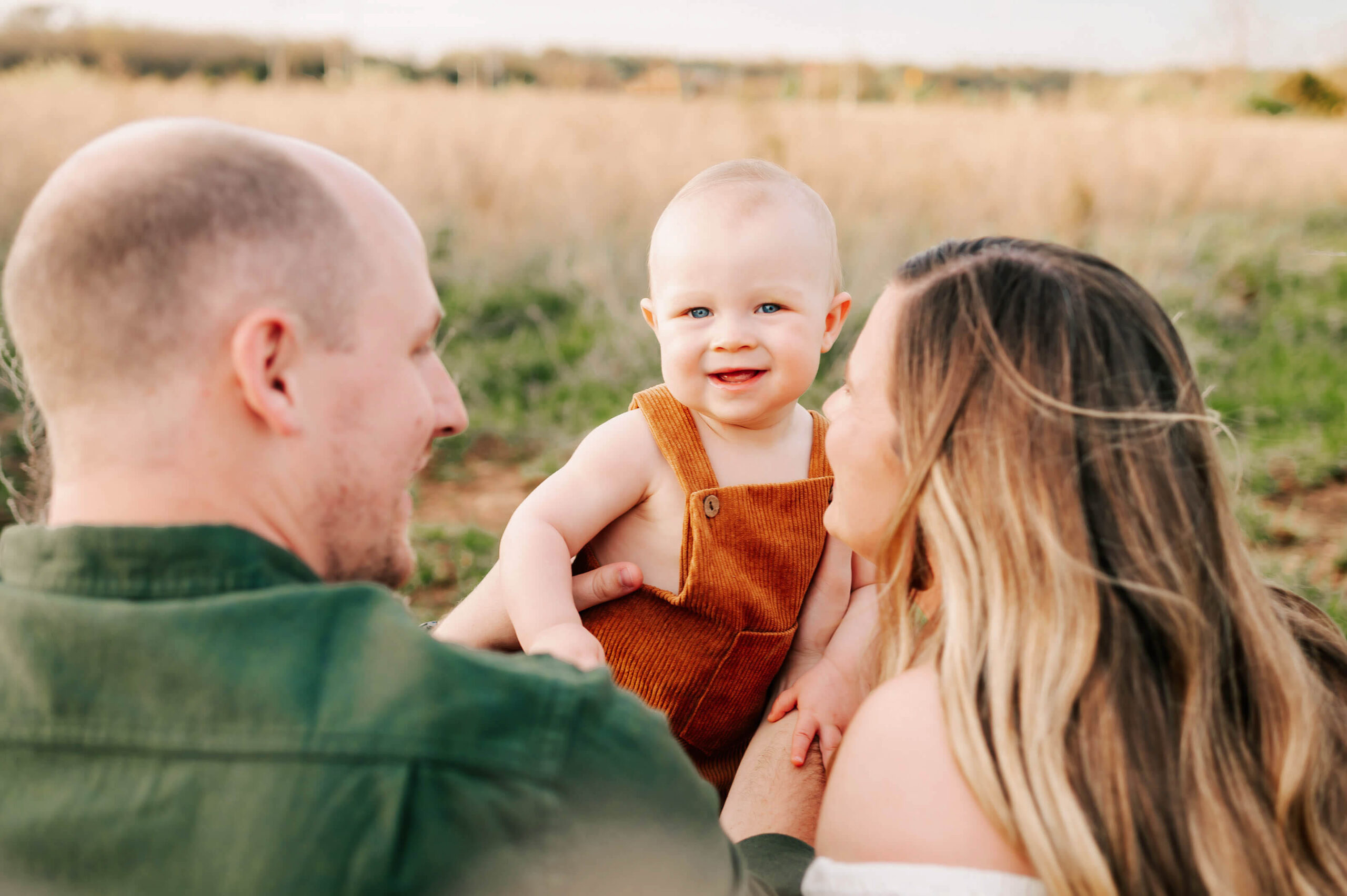 parents holding baby boy in field captured by Springfield MO family photographer Jessica Kennedy of The XO Photography