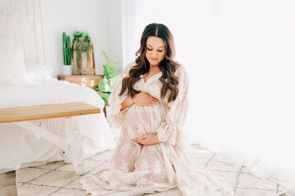Kansas city maternity photographer captures pregnant mom kneeling in photography studio in lace dress