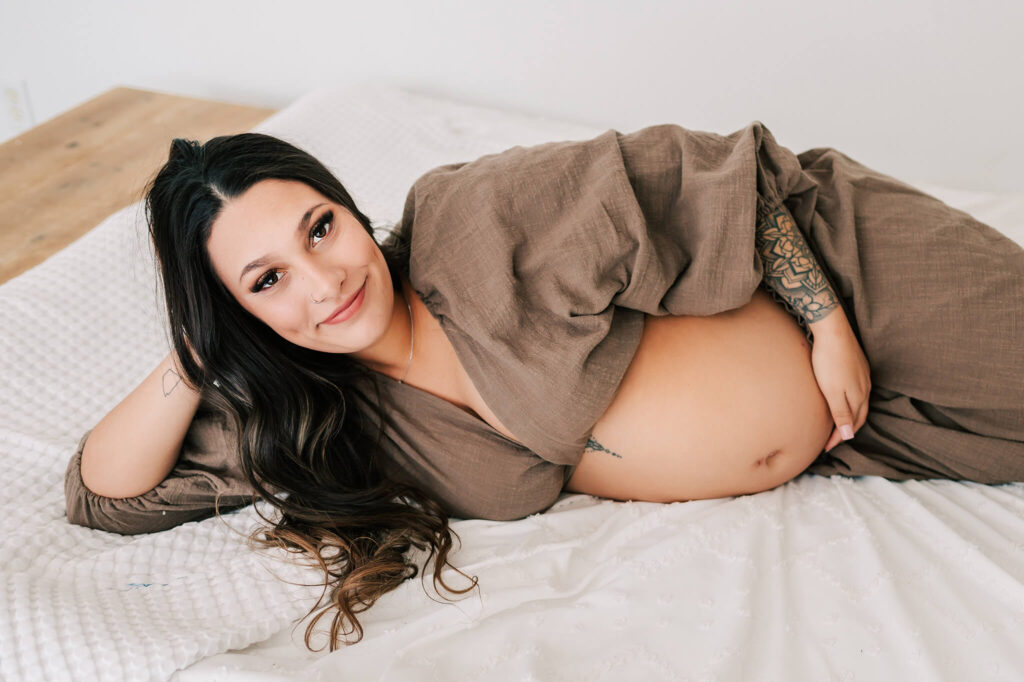 Maternity photographer in kansas city captures mom laying in bed holding baby bump