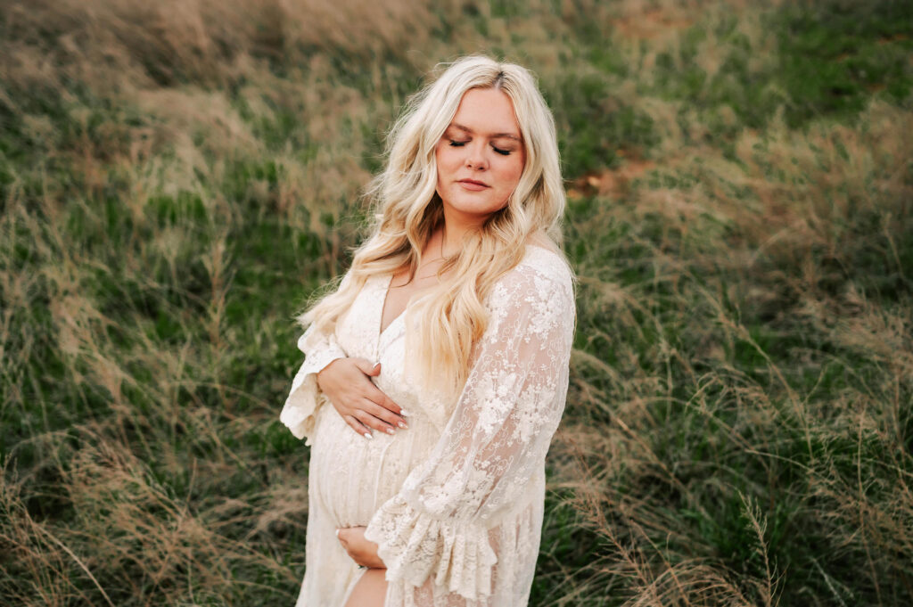 pregnant mom in lace dress holding baby bump in field in Kansas City