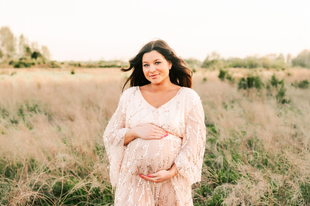 pregnant mom standing in field during Kansas City maternity photography session with wind in her hair