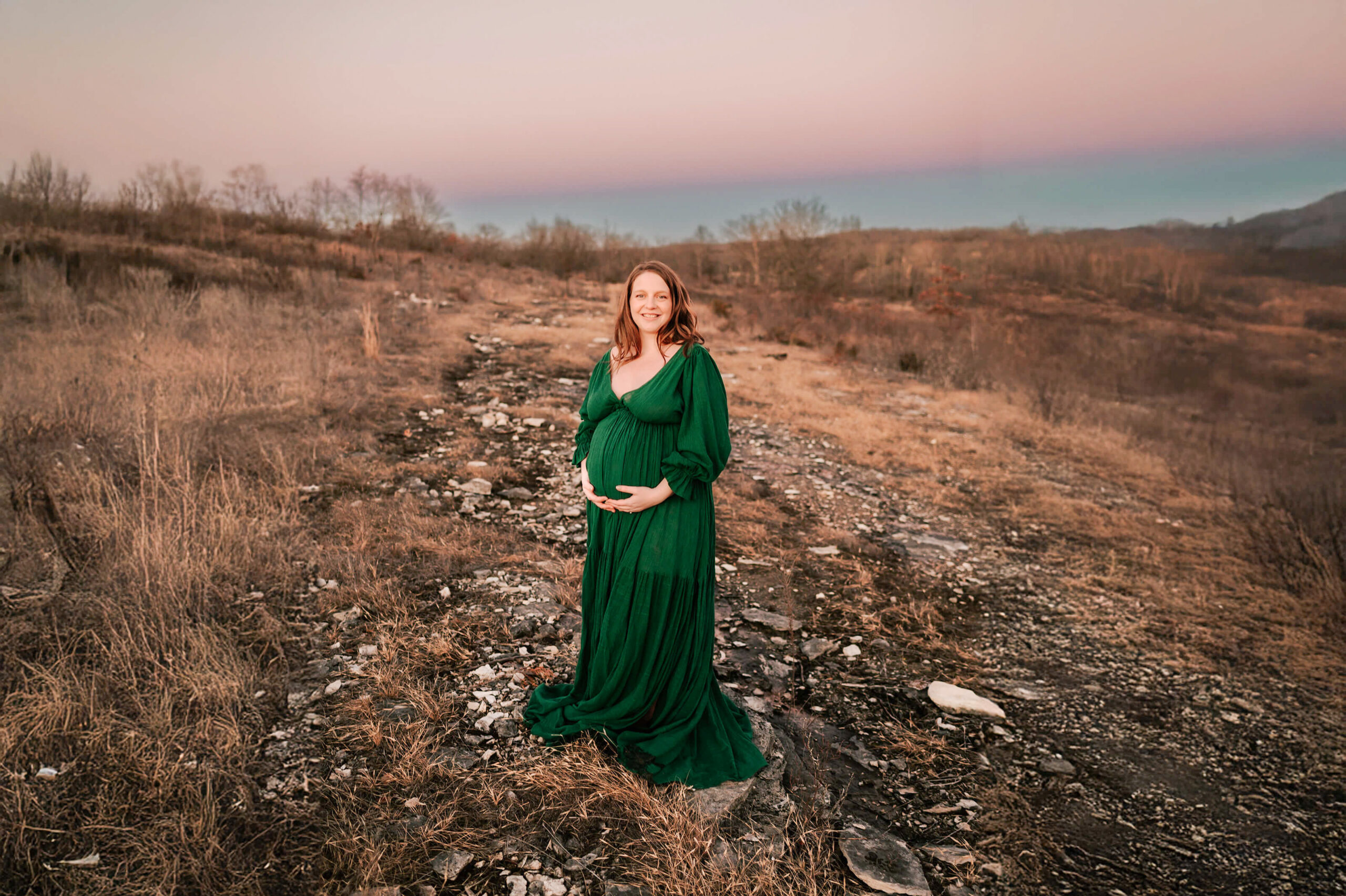 pregnant mom standing on hillside holding baby bump during Springfield MO maternity photography session