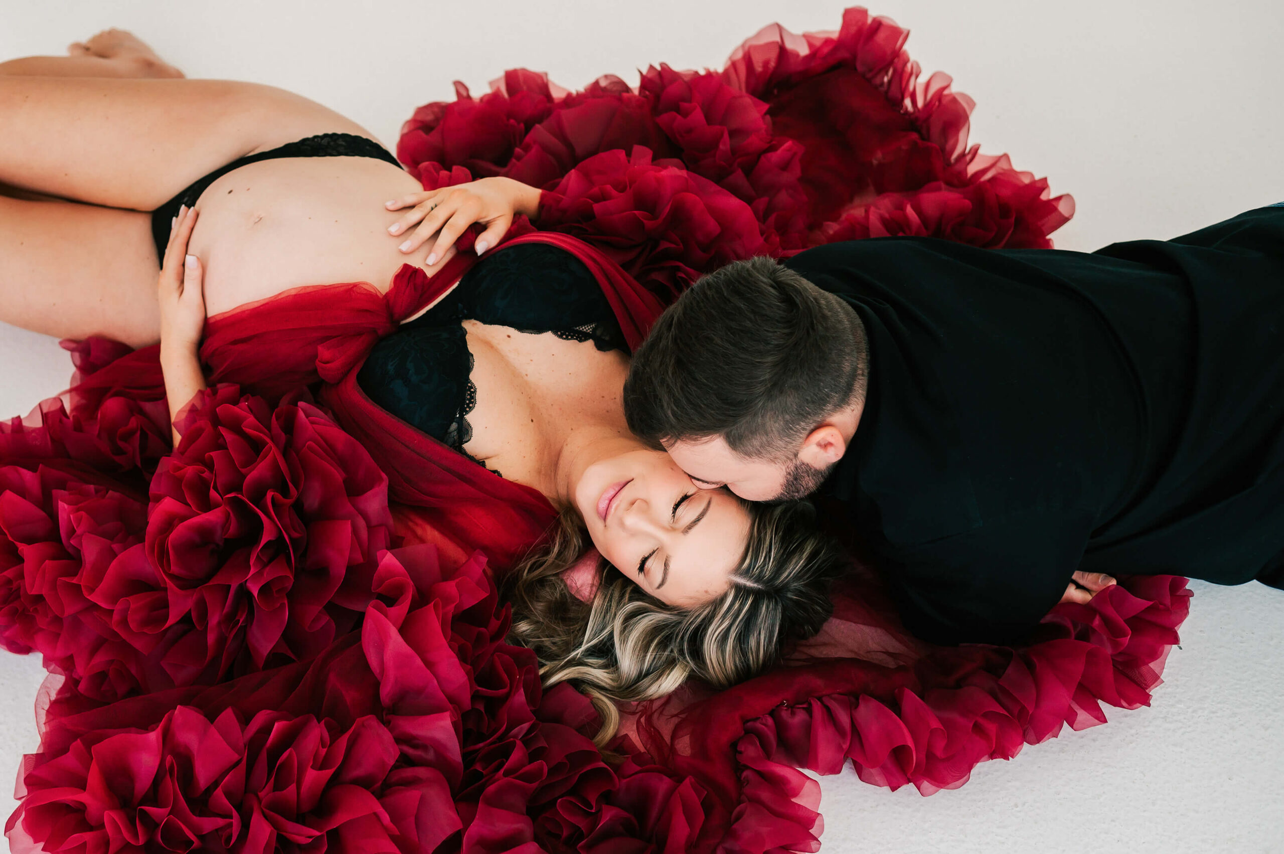 Kansas City maternity photographer captures pregnant mom laying on the ground of studio kissed by her husband